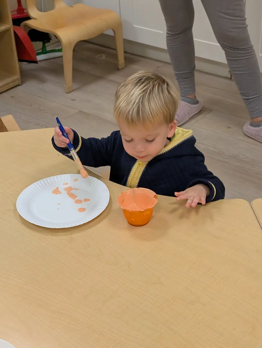 A toddler painting with a brush at the art table at Blossom Station