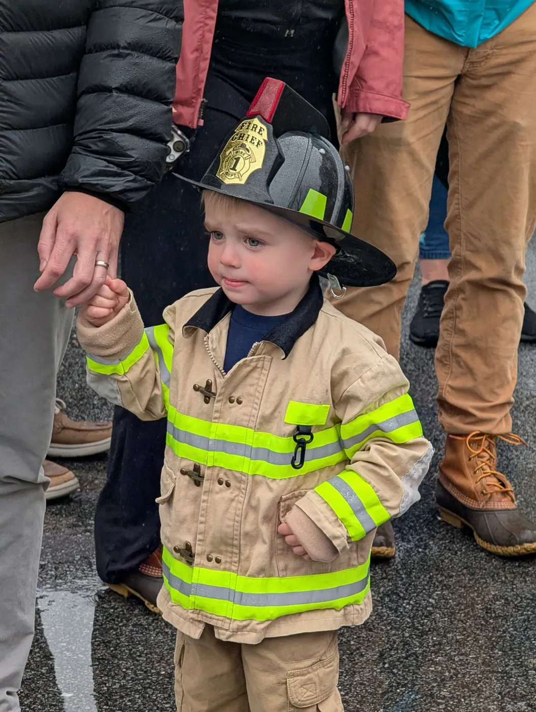 A toddler in a firefighter costume holding a grown-up's hand at the Blossom Station Halloween Parade
