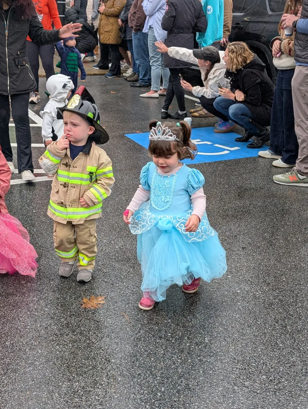 A firefighter and a princess lead the procession as families cheer from the parking lot at Blossom Station's Halloween Parade