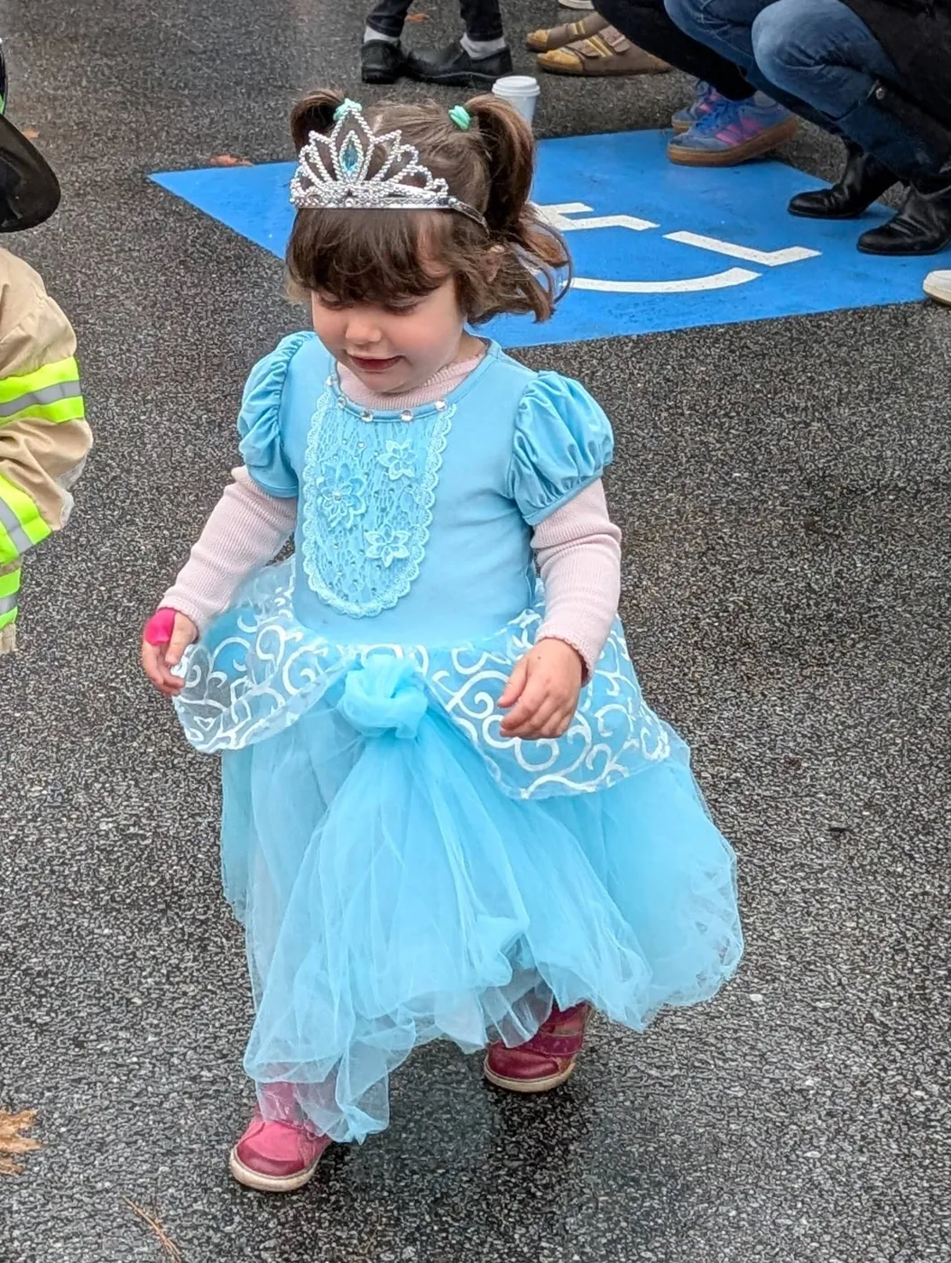 A toddler in a blue princess dress and tiara walking the Halloween Parade route at Blossom Station