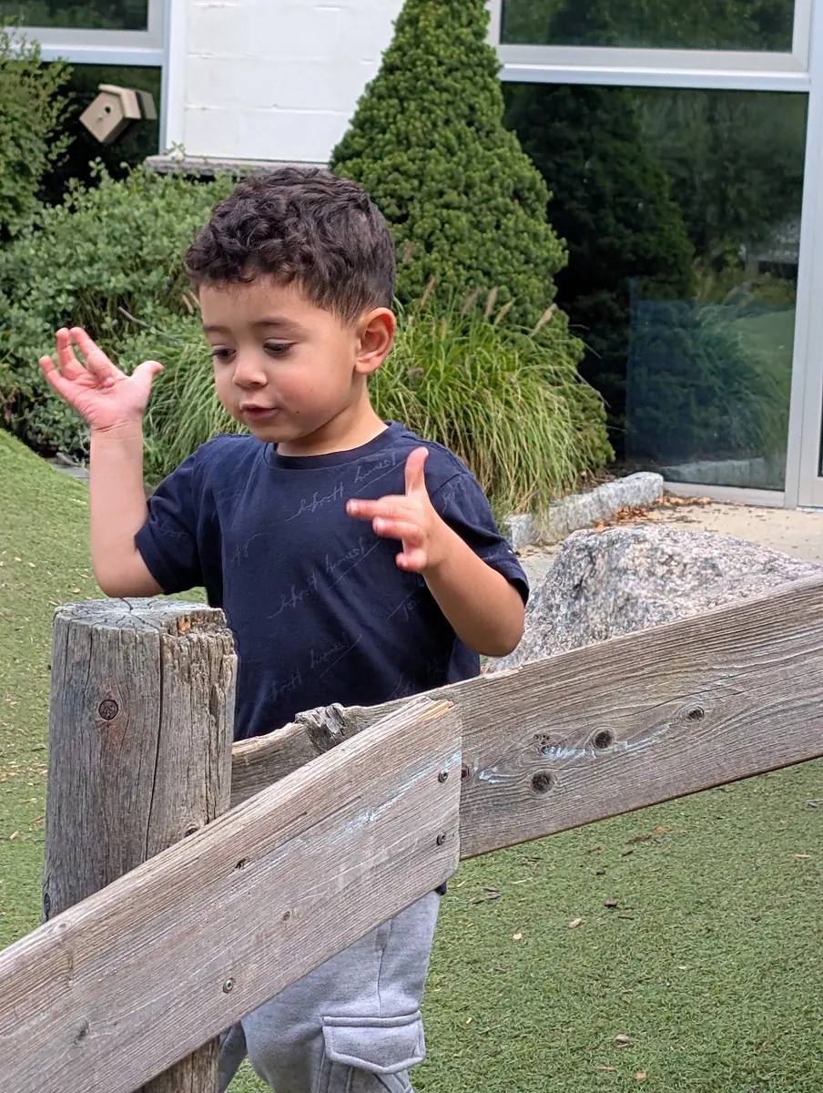 A toddler exploring a natural wooden fence and rocks outdoors at Blossom Station in Acton, MA