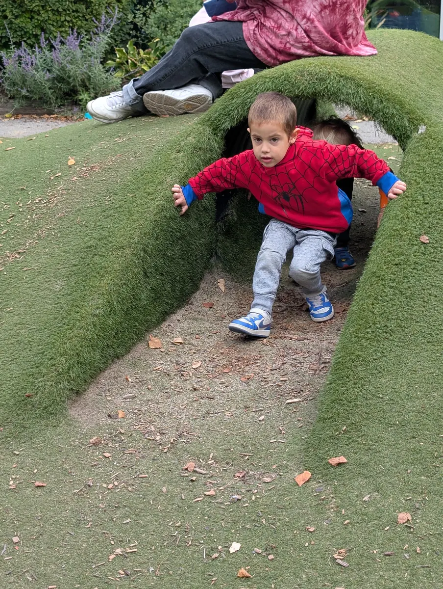 A preschooler crawling out of the grass tunnel on the Blossom Station playground