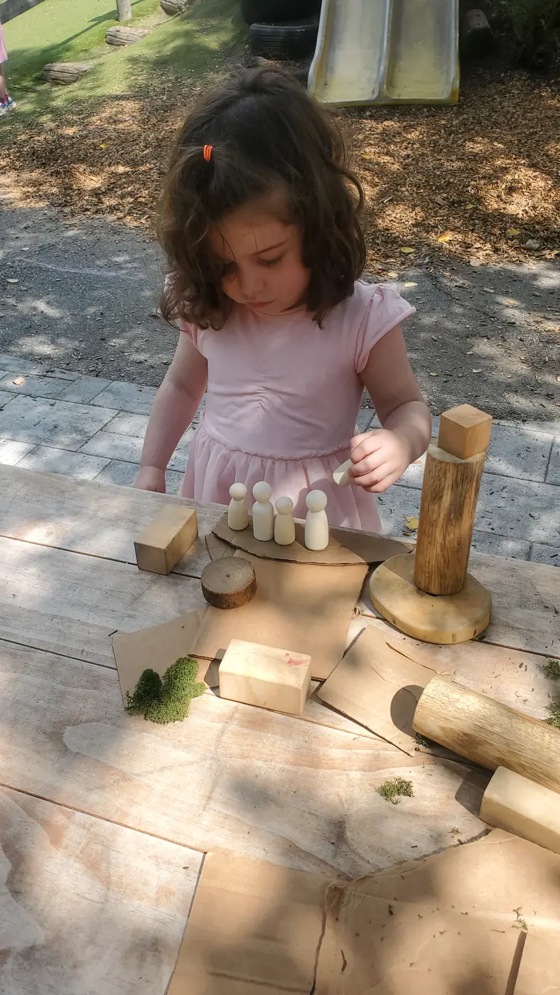 A child building with wooden loose parts, blocks, and moss during TimberNook outdoor play at Blossom Station in Acton, MA