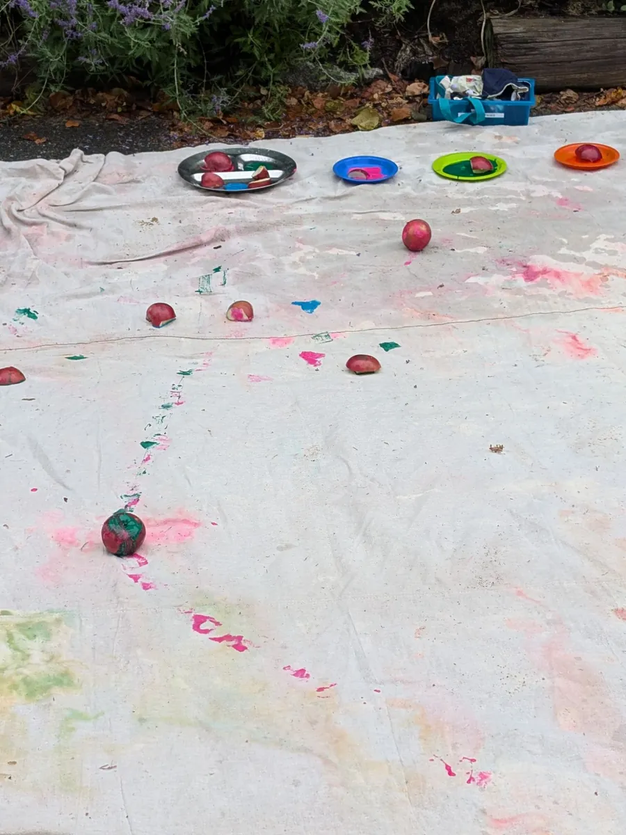 Apple halves dipped in paint and colorful apple prints across a canvas at TimberNook Apple Day