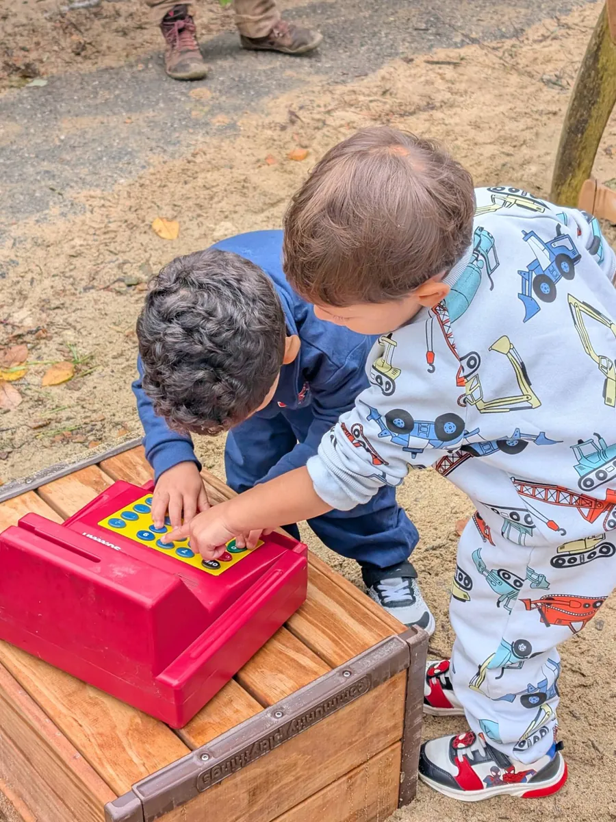Two toddlers pressing the buttons on a toy cash register at the TimberNook pretend apple shop
