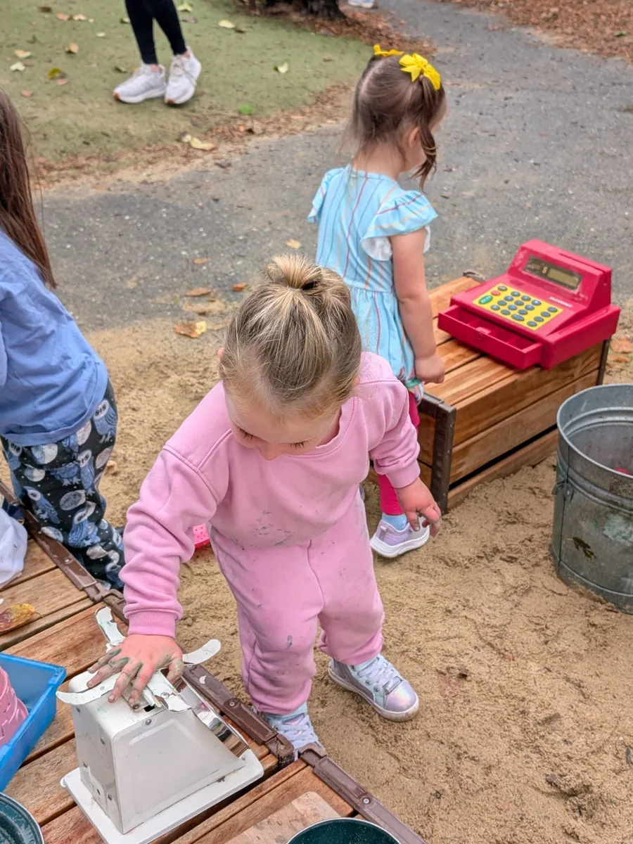 A preschooler working an old kitchen scale at the apple shop while a friend runs the toy cash register