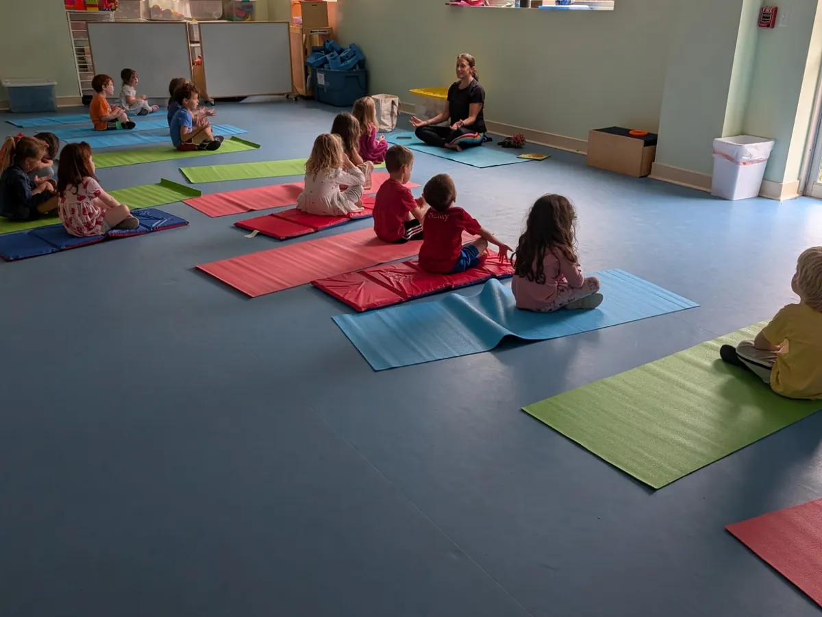 A full yoga class of preschoolers sitting cross-legged on mats in the Blossom Station movement room