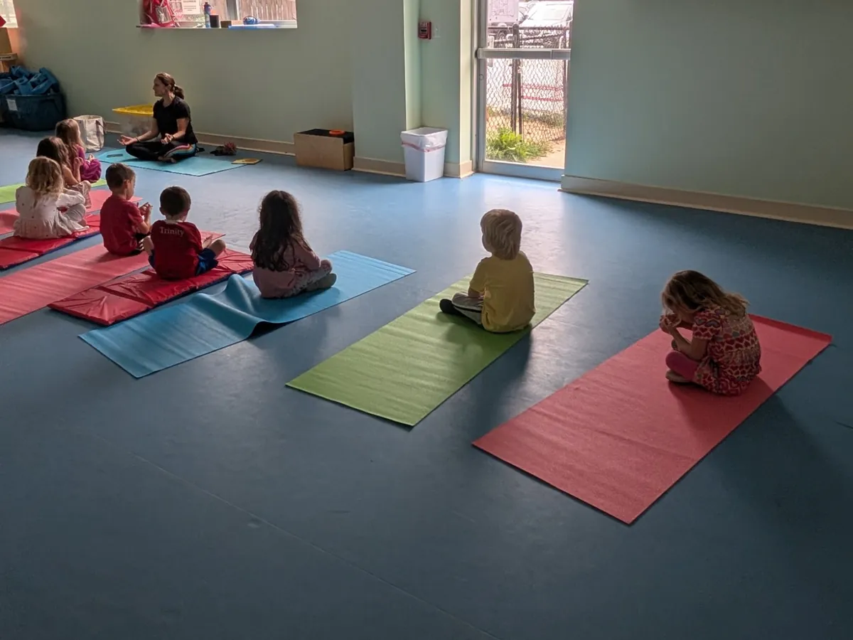 Children sitting on red, green, and blue yoga mats following their instructor at Blossom Station